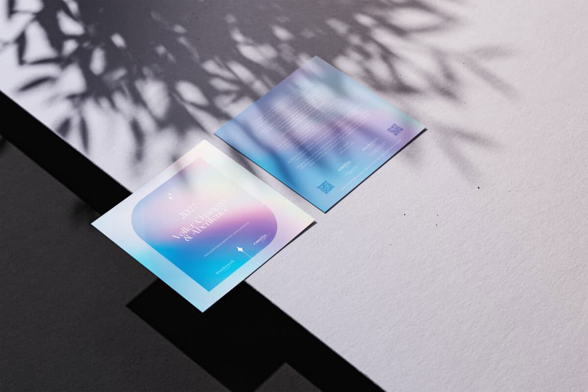 Zwei bunte Postkarten auf einem Tisch mit Schatten und Blättern.